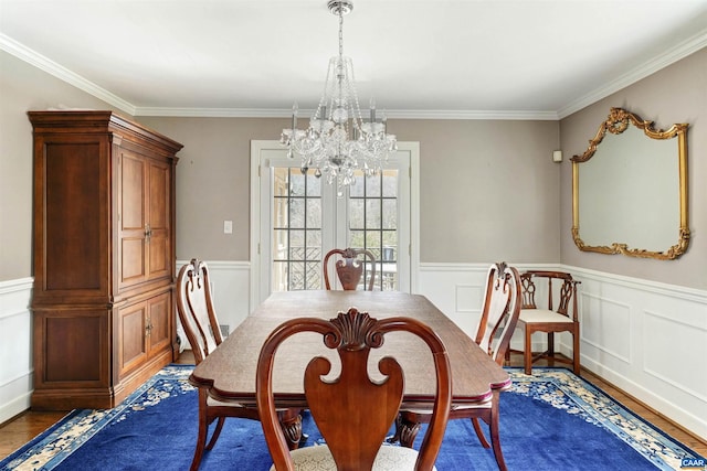 dining room featuring crown molding, wainscoting, a notable chandelier, and wood finished floors