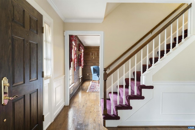 foyer entrance with ornamental molding, a decorative wall, stairway, and wood finished floors