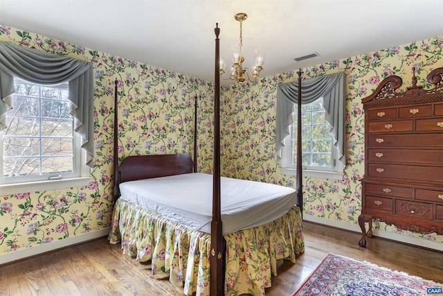 bedroom with multiple windows, wood finished floors, visible vents, and wallpapered walls