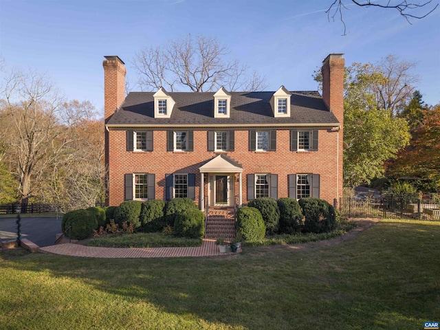 georgian-style home with fence, a chimney, and a front lawn