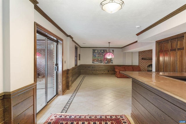 kitchen with light tile patterned floors, a wainscoted wall, ornamental molding, decorative light fixtures, and a brick fireplace