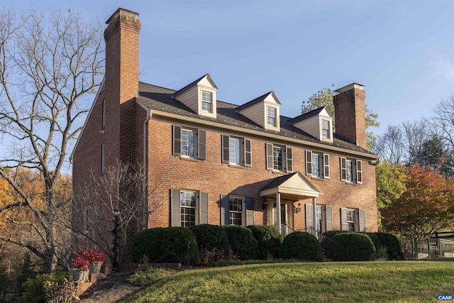 colonial home with brick siding, a chimney, and a front lawn