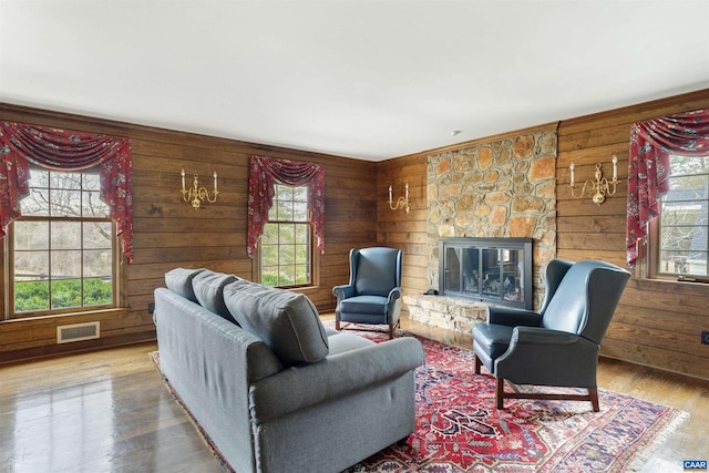 living area featuring visible vents, wood walls, a stone fireplace, and wood finished floors