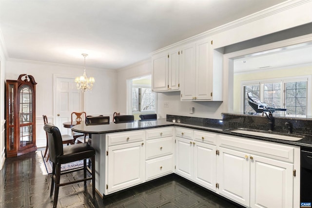 kitchen with ornamental molding, white cabinetry, a sink, a chandelier, and a peninsula