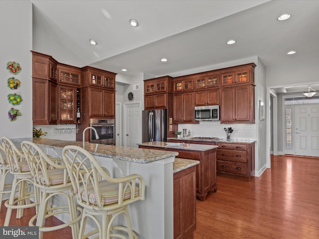 kitchen with a peninsula, a breakfast bar, wood finished floors, appliances with stainless steel finishes, and decorative backsplash