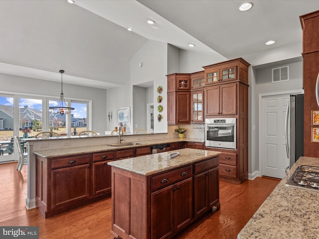 kitchen featuring visible vents, a peninsula, light stone countertops, stainless steel appliances, and a sink