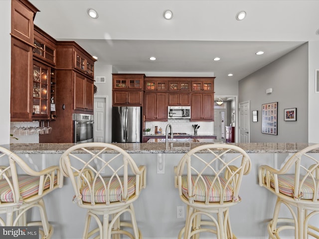 kitchen featuring tasteful backsplash, glass insert cabinets, stainless steel appliances, and a breakfast bar area