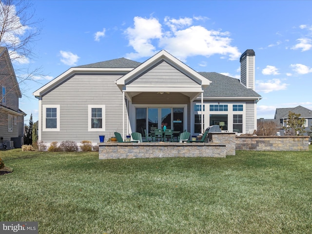 rear view of property featuring a shingled roof, a patio area, a yard, and a chimney