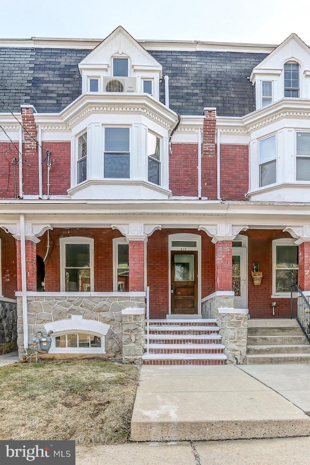 view of front of property featuring a porch, brick siding, and mansard roof