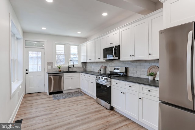 kitchen with dark countertops, light wood-style flooring, appliances with stainless steel finishes, white cabinets, and a sink