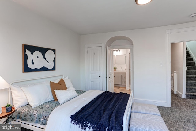 bedroom with arched walkways, light carpet, a sink, ensuite bath, and baseboards