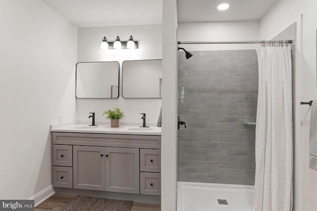 full bathroom featuring double vanity, a shower stall, a sink, and wood finished floors