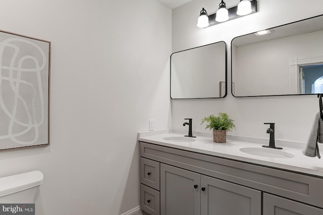 full bathroom with toilet, double vanity, and a sink