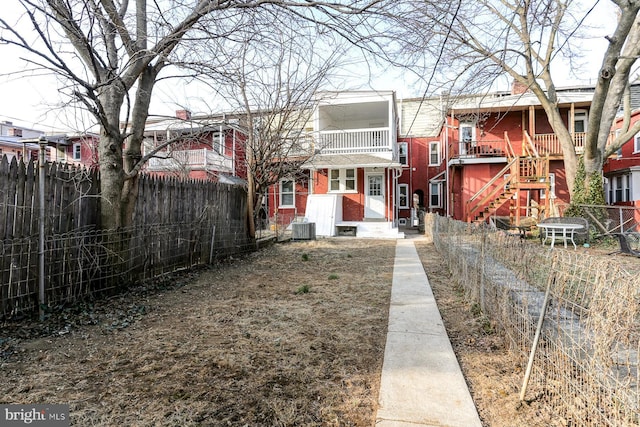 rear view of property with a fenced backyard, central AC, and a balcony