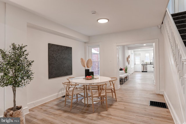 dining room featuring light wood-style floors, visible vents, baseboards, and stairs