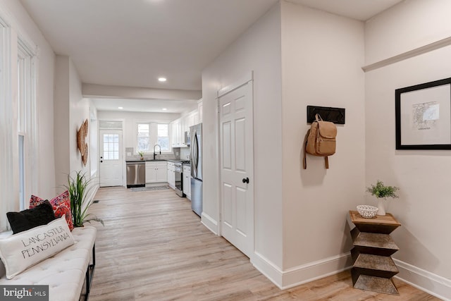 corridor with recessed lighting, light wood-type flooring, a sink, and baseboards