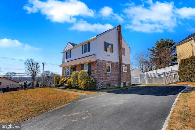 view of front facade featuring a front yard, brick siding, fence, and a chimney