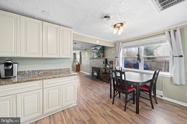 dining area with light wood-style flooring, a fireplace, visible vents, and baseboards