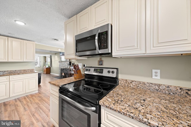 kitchen with light stone counters, light wood-style floors, appliances with stainless steel finishes, and a textured ceiling