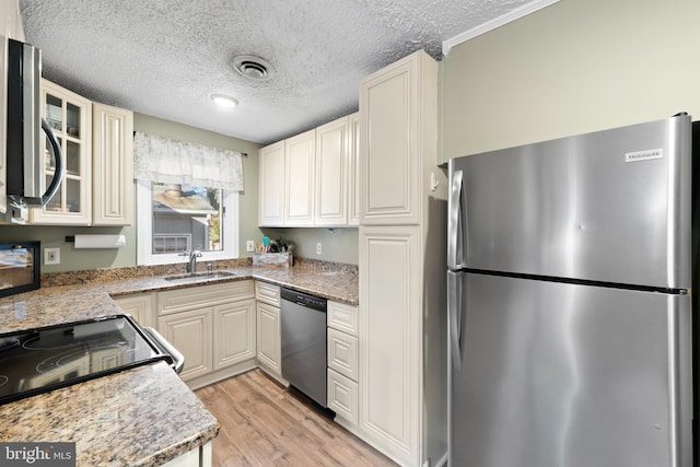 kitchen featuring visible vents, a sink, light wood-style floors, appliances with stainless steel finishes, and glass insert cabinets