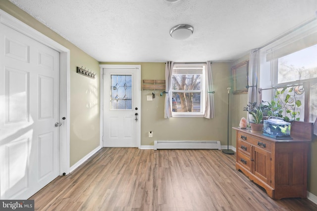 foyer entrance featuring a wealth of natural light, a baseboard heating unit, light wood-style floors, and a textured ceiling