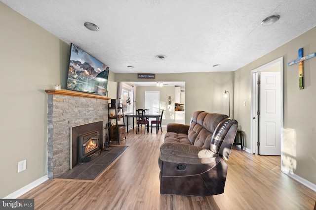 living area with wood finished floors, visible vents, baseboards, a stone fireplace, and a textured ceiling