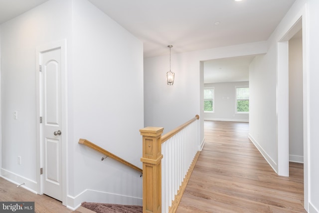 corridor with light wood finished floors, baseboards, and an upstairs landing