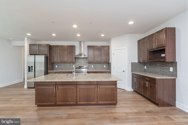 kitchen with tasteful backsplash, appliances with stainless steel finishes, light wood-style floors, wall chimney range hood, and an island with sink