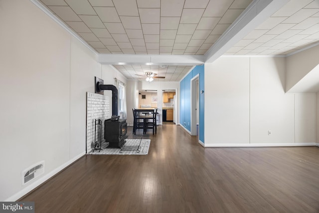 interior space with visible vents, ceiling fan, dark wood-type flooring, a wood stove, and crown molding