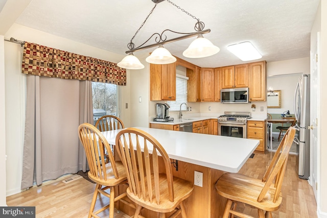 kitchen with light countertops, appliances with stainless steel finishes, a sink, light wood-type flooring, and a kitchen bar