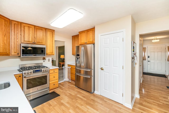 kitchen featuring stainless steel appliances, brown cabinetry, light countertops, and light wood finished floors