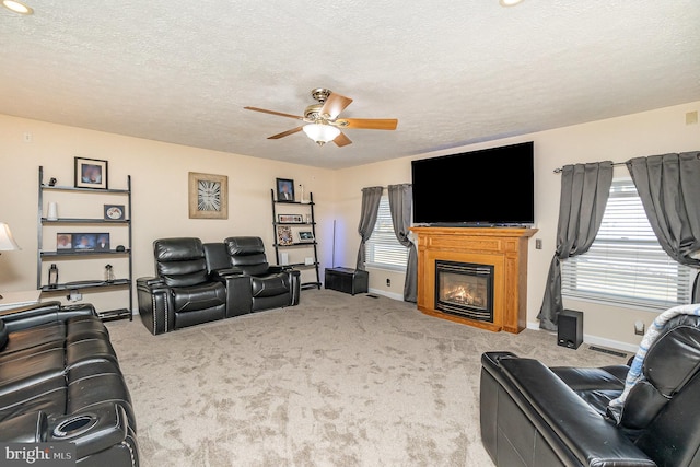 carpeted living area with a textured ceiling, a glass covered fireplace, a ceiling fan, and baseboards