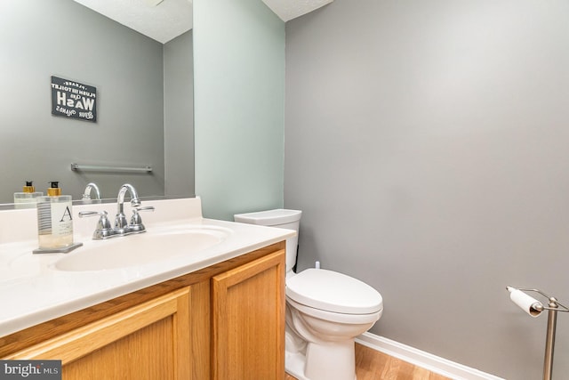 half bathroom featuring baseboards, vanity, toilet, and wood finished floors