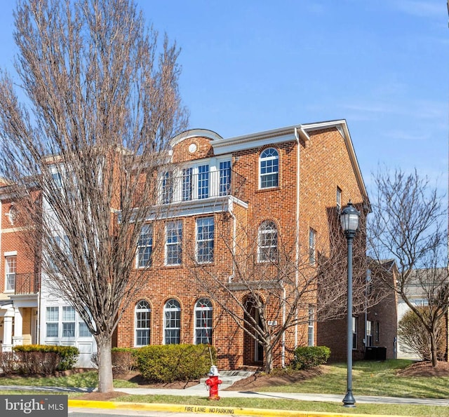 view of front of home with brick siding, a front lawn, and a balcony