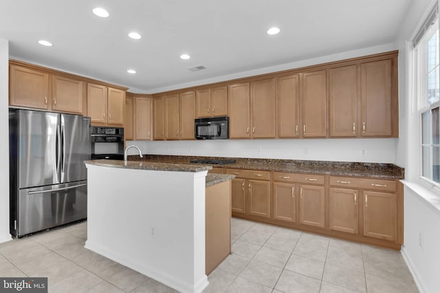 kitchen featuring dark stone counters, a kitchen island with sink, light tile patterned flooring, black appliances, and recessed lighting