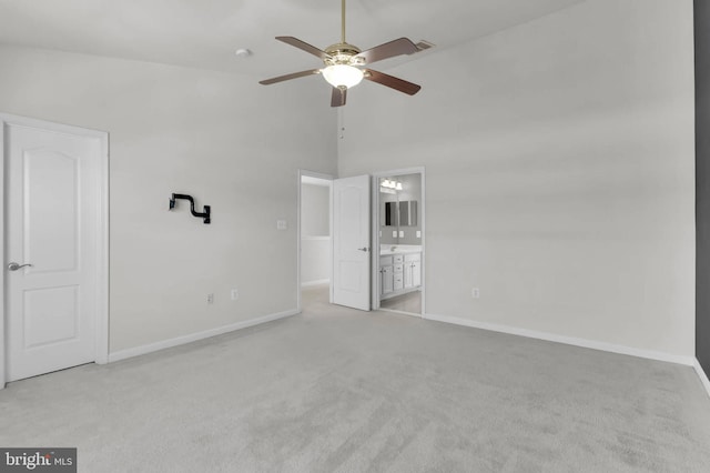 unfurnished bedroom featuring a towering ceiling, light colored carpet, ensuite bath, and baseboards