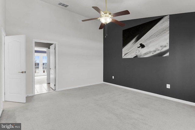 empty room with baseboards, visible vents, ceiling fan, a high ceiling, and carpet flooring