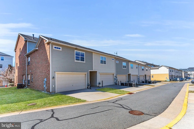 townhome / multi-family property featuring a garage, a residential view, brick siding, and a front yard