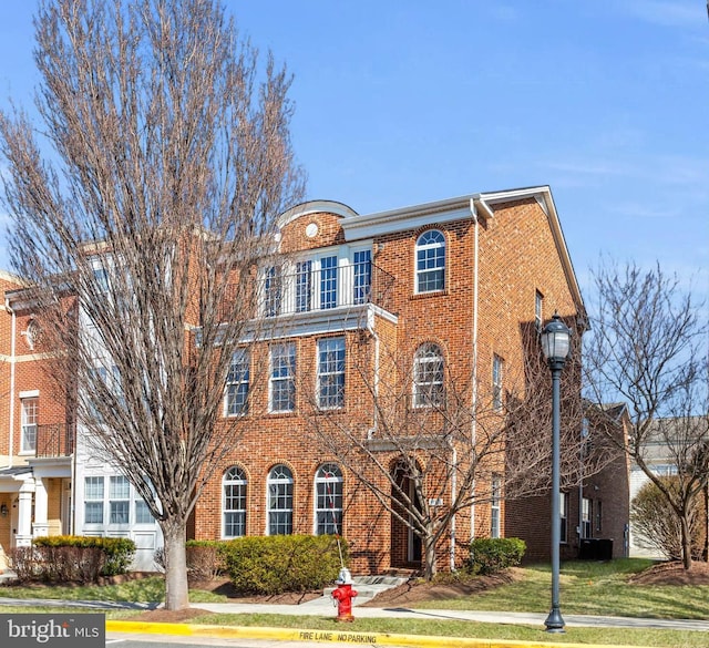 view of front of property with a front yard, brick siding, and a balcony