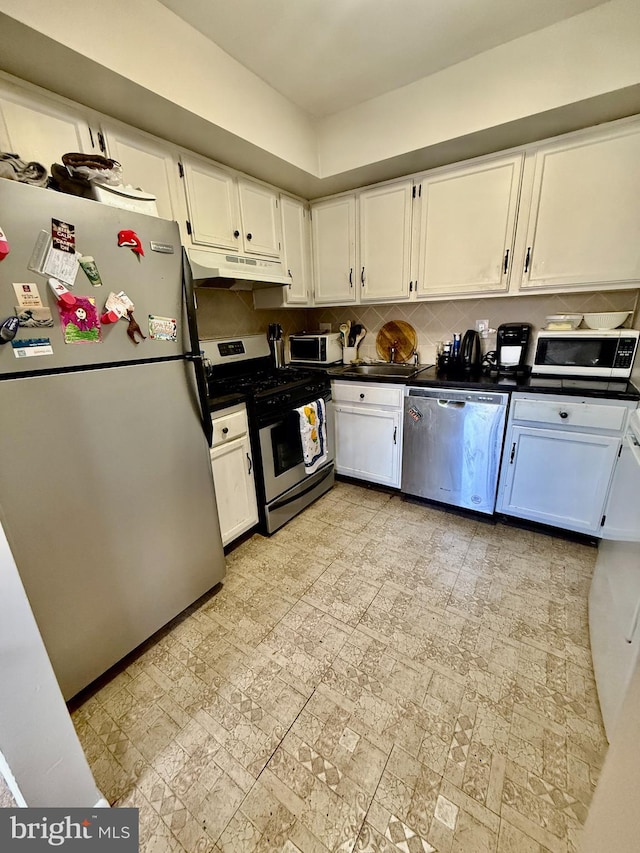 kitchen with dark countertops, under cabinet range hood, appliances with stainless steel finishes, and white cabinets