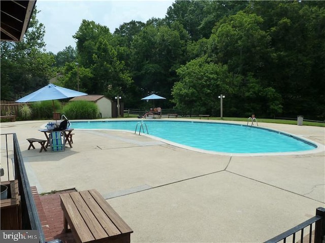 community pool with an outbuilding, a patio, a storage shed, and fence