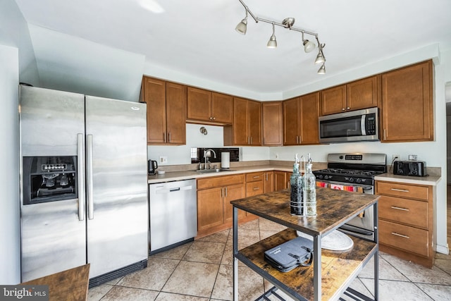 kitchen featuring light tile patterned floors, stainless steel appliances, a sink, light countertops, and brown cabinetry