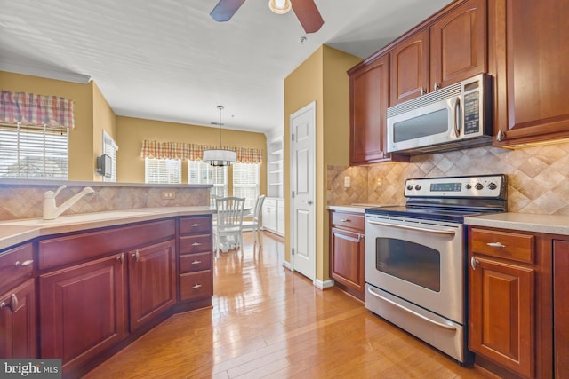 kitchen with backsplash, light countertops, appliances with stainless steel finishes, light wood-style floors, and a sink