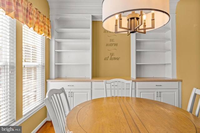 unfurnished dining area featuring built in features, a notable chandelier, baseboards, and ornamental molding