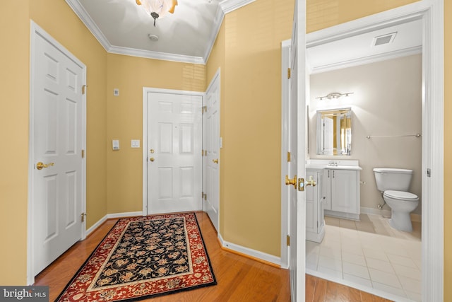 foyer entrance with crown molding, wood finished floors, visible vents, and baseboards