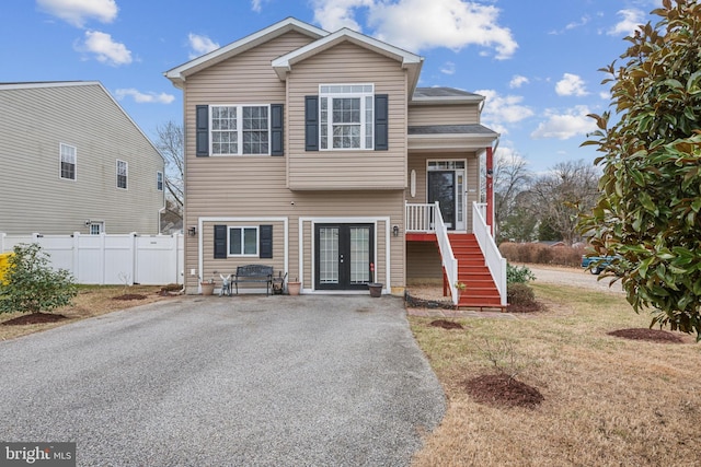 tri-level home featuring french doors, stairway, a front lawn, and fence