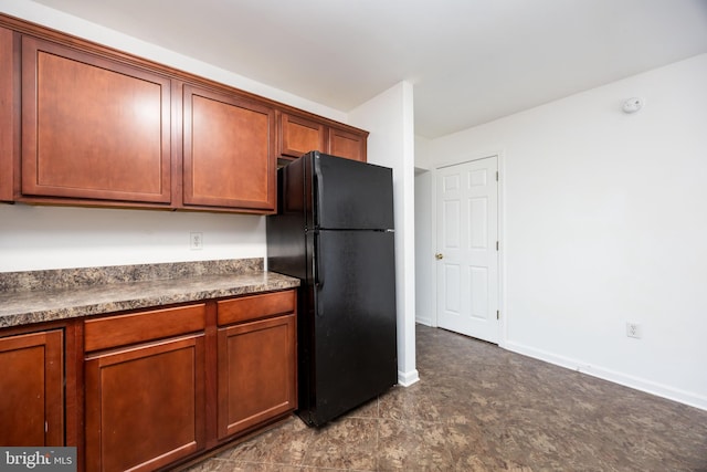 kitchen featuring dark countertops, brown cabinetry, baseboards, and freestanding refrigerator