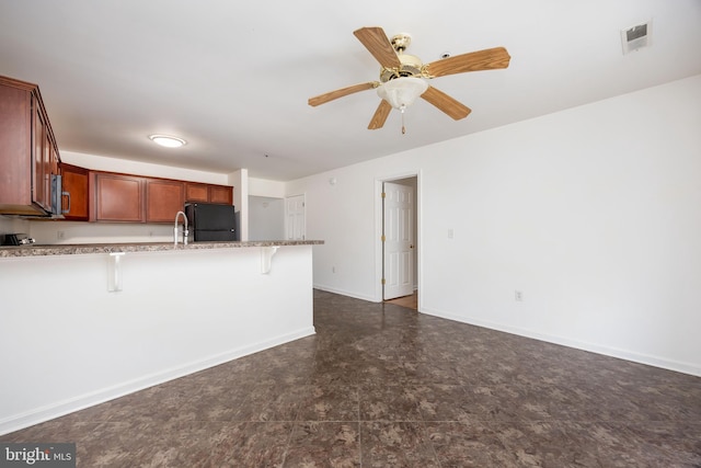 kitchen with a kitchen bar, stainless steel microwave, freestanding refrigerator, a peninsula, and baseboards