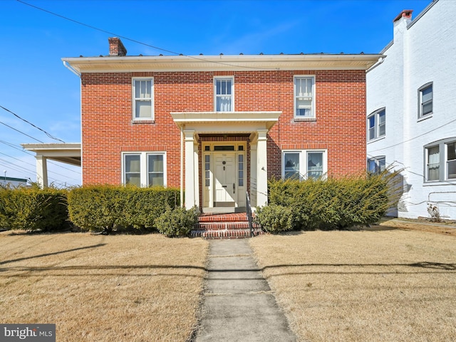 view of front of property with a front yard, brick siding, and a chimney