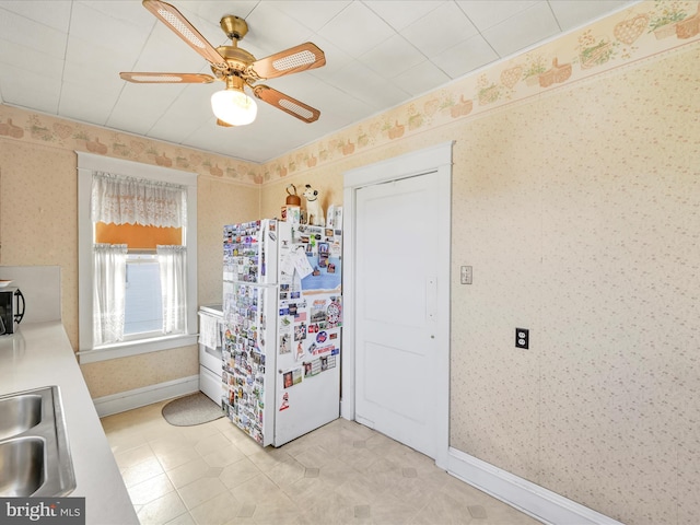 kitchen featuring freestanding refrigerator, ceiling fan, a sink, baseboards, and wallpapered walls